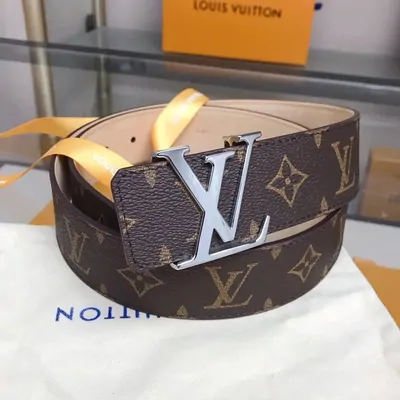 Brown monogram belt with a silver initial buckle, resting on a cloth dust bag