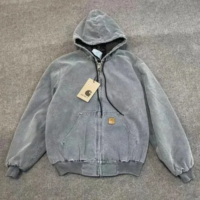 Grey washed zip-up hooded work jacket with a paper tag still attached, laid flat on carpet