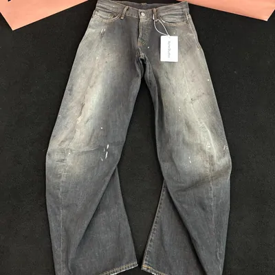 Faded wide-leg distressed jeans flat on a dark floor, a tag still at the waistband