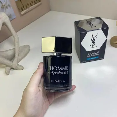 A hand holding a dark glass fragrance bottle with a gold cap, its box standing behind