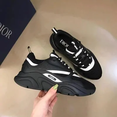 Black and white low-top sneakers, one standing on its box and one held up in a hand