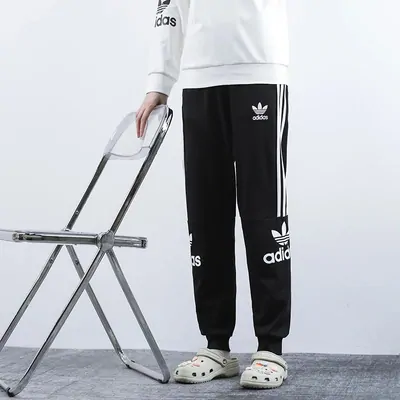 Black track pants with three stripes down each leg, worn, beside a clear plastic chair