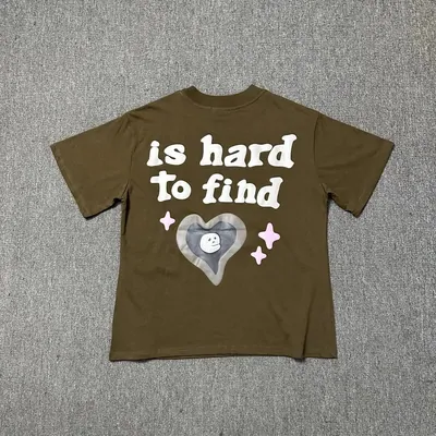 Brown t-shirt laid flat on concrete, the back print reading is hard to find above a heart