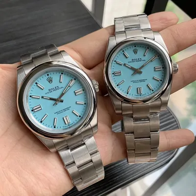 Two steel bracelet watches with turquoise dials, held up in two hands